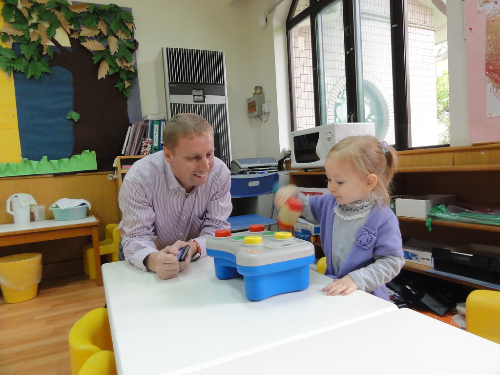 A caregiver and a young child playing together with an activity toy in a childcare classroom.