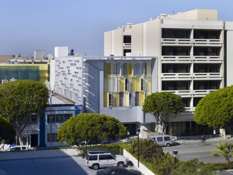 Exterior of a modern multi-story supportive housing apartment building with trees along the sidewalk.